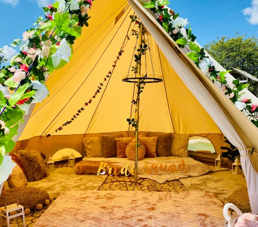 Bell tent entrance with floral garlands, cushions and a low table